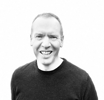 Black and white head and shoulders photo of Matt Stevenson-Dodd. Matt is smiling and wearing a dark jumper