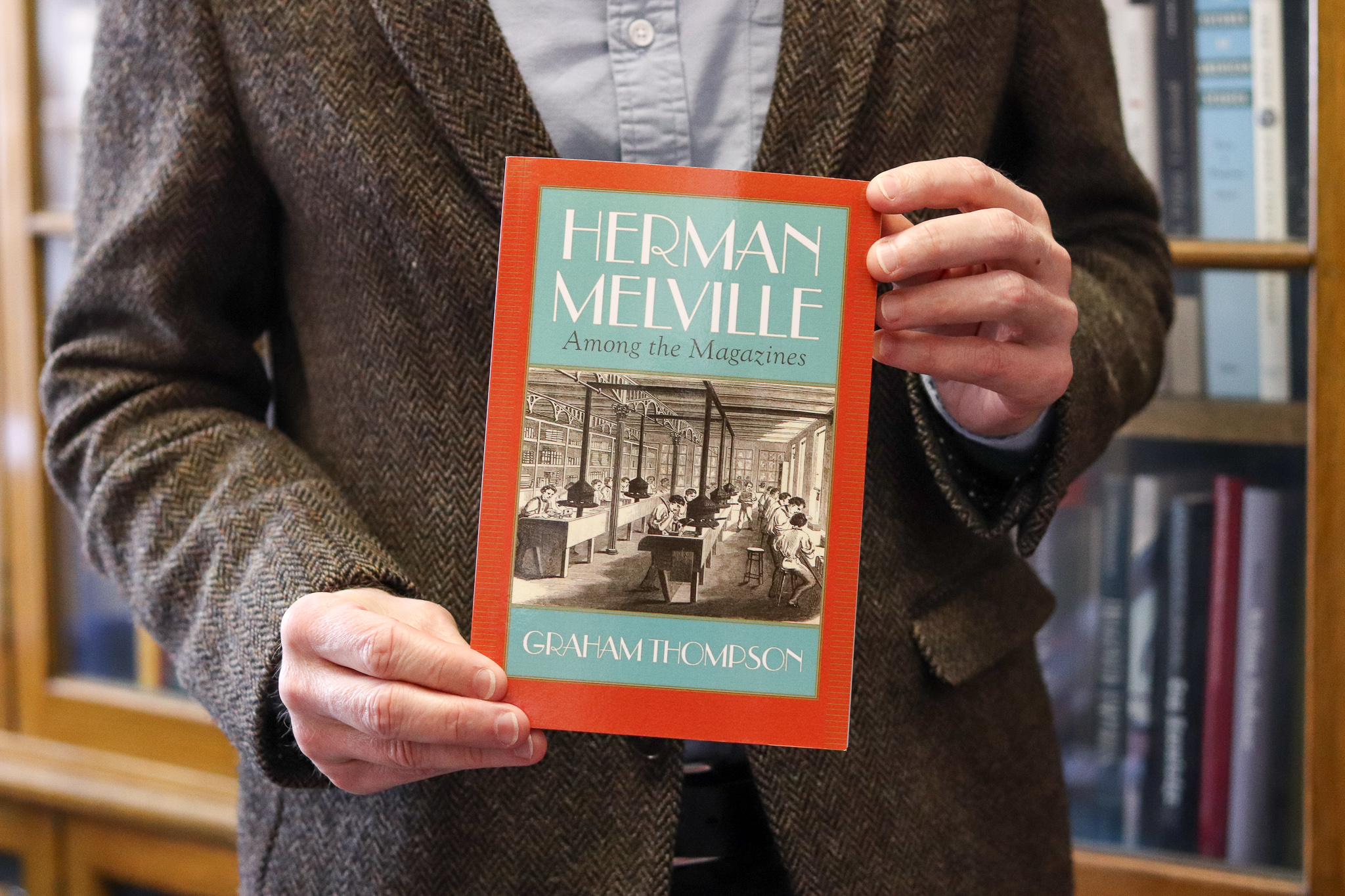 A cropped image of a man holding a book entitled 'Herman Melville: Among the Magazines'.