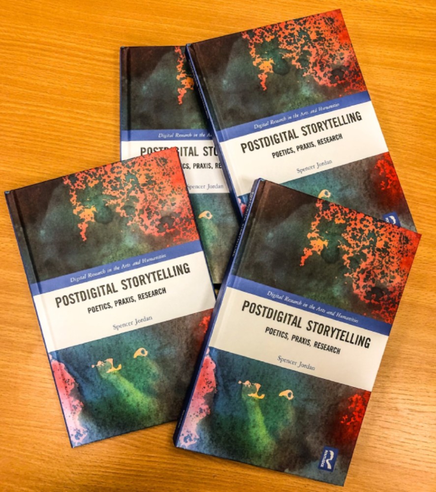 Four copies of Spencer Jordan's book Postdigital Storytelling: Poetics, Praxis and Research, photographed from above.