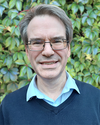 Head and shoulder photo of Stephen Timmons. Stephen is wearing glasses, a navy jumper and a light blue collared shirt.
