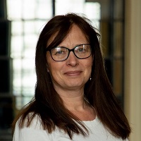 Photo of Julia Conns. Julie has shoulder length dark hair with a fringe and is wearing a white top and glasses.
