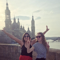 Two girls in sunglasses pose on a hot day, on a bridge with a cathedral in the background