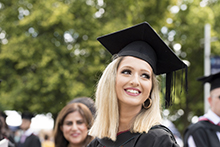 Head and shoulders shot of a graduate in cloak and mortar board, she smiles looking over her shoulder