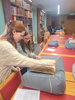 Two students looking at a manuscript rested on a cushion in a library.