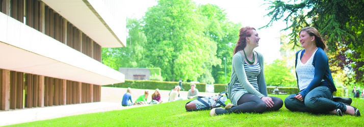 Two female undergraduate students sitting on grass outside Hallward Library, University Park 714x249