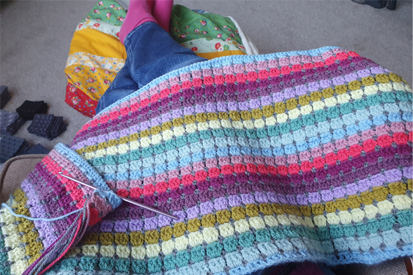 A close up image of a brightly coloured crochet blanket in progress with crochet needle and strands of wool