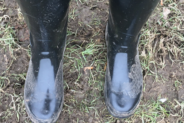 A close up image of someone walking through a muddy field in a pair of black muddy wellies in lockdown