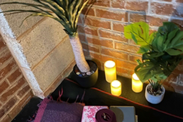 An image showing plants, lighted candles and yoga props - yoga blanket, yoga blocks - with a brick wall backdrop