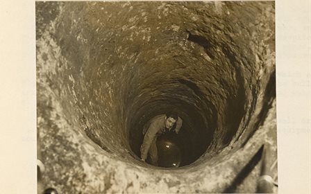 Historical photo of a person peering up from a vertical cave shaft.