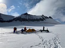 Group of people and tents pitched in the middle of a large expanse of snow.