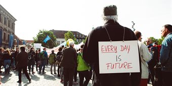 Older man stood in a crowd wearing a banner which reads every day is future