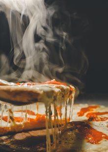 A slice of pizza being pulled from the pizza with melted cheese