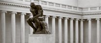 The Thinker statue, a bronze statue of a man with his elbow on his knee and chin resting on his fist outside a building