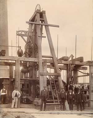 Photograph showing a large wooden-frame pump mechanism, surrounded by workmen