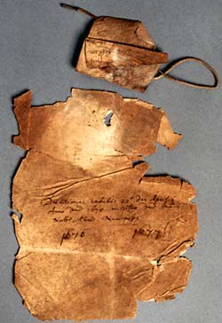 A bundle cover, discoloured and much damaged around the edges, and the parchment tag that was used to attach the pages.
