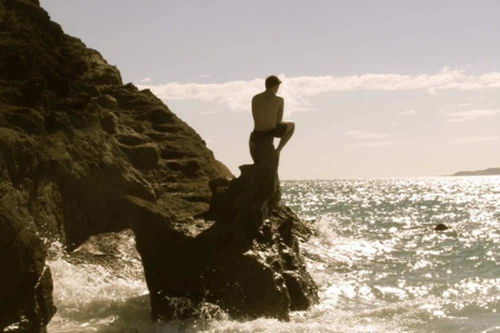 Man sitting on rocks staring out to sea
