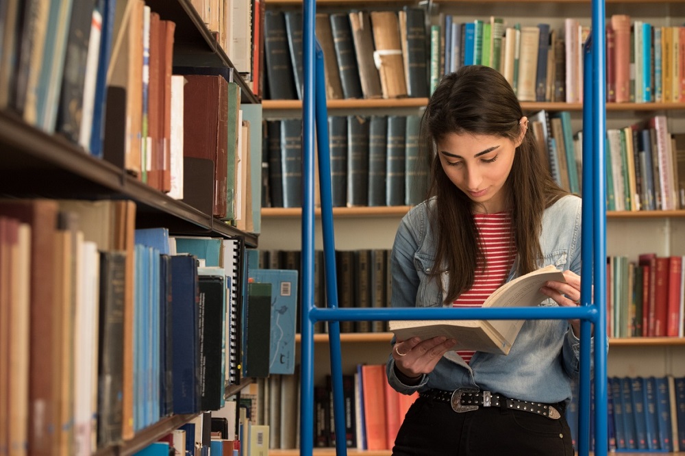 Researcher standing on ladder in library reading a book