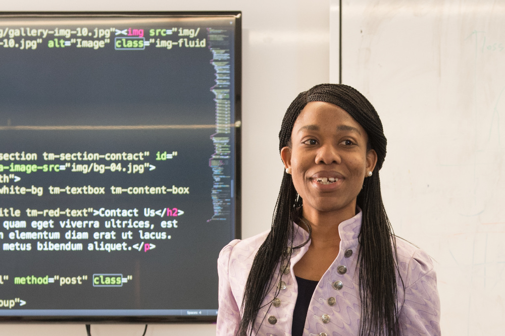 Black woman presenting with screen of code behind her