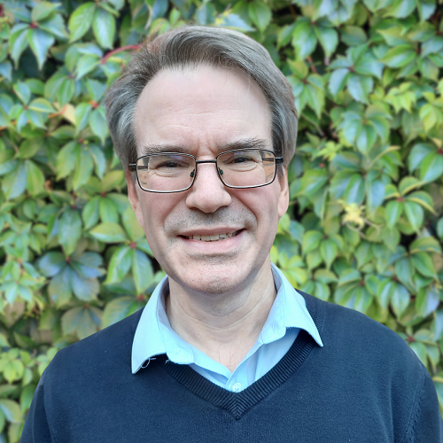 Head and shoulders photo of Stephen Timmons. Stephen is wearing glasses, a dark navy jumper and a pale blue shirt.
