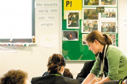 A teacher wearing a green cardigan helping a student in the middle of a lesson.