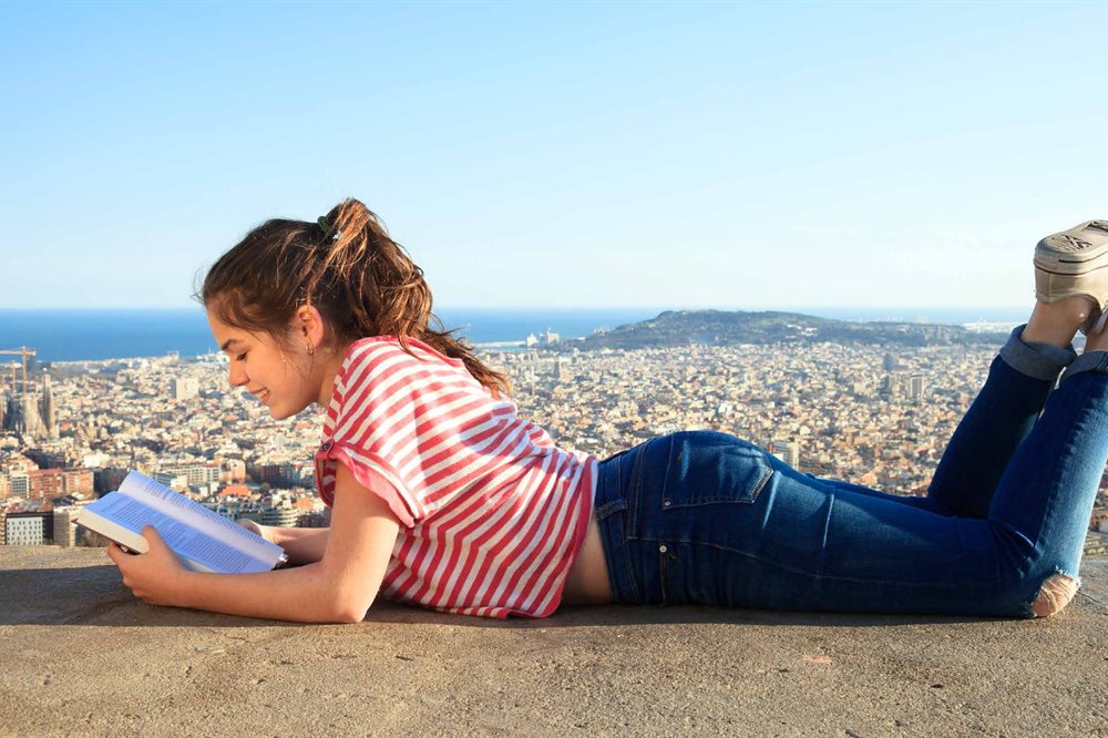 Student reading a book while overlooking a city with the sea in the background