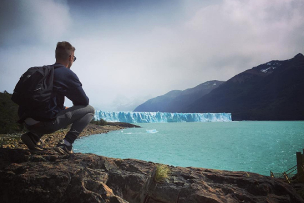 Student crouched by side of lake looking at glacier