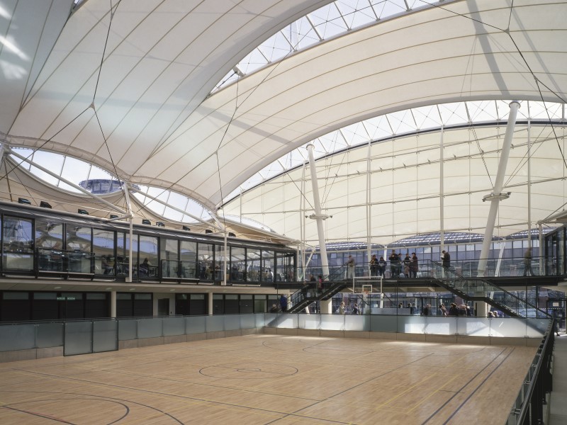 A view of the finished Castle Meadow Campus from inside the Central building with people networking on balcony and a basketball court