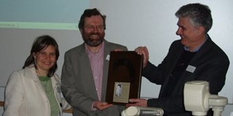 Two men and a woman smile as the man in the centre is presented with a plaque