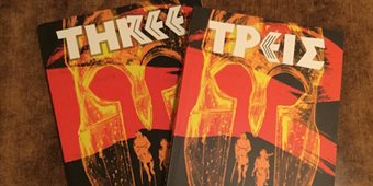Two copies of the graphic novel 'Three' displaying a Spartan warrior's helmet on the covers.