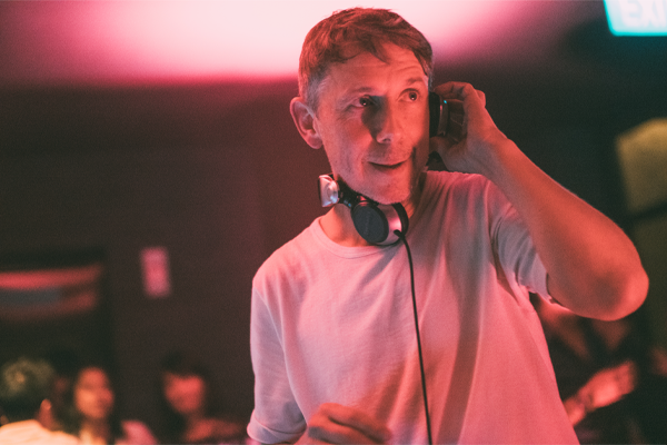 A photo of Gilles Peterson with his headphones around his neck holding the left headphone to up his left ear