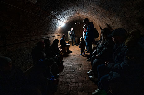 A tour guide talking to visitors in a brick-walled circular tunnel.