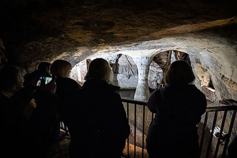 Silhouettes of visitors next to a railing overlooking sandstone cave features lit in the background.