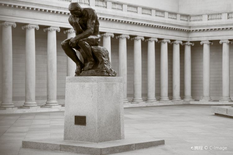 'The Thinker' by Rodin - image shows a bronze statue on a marble plinth of a man resting his chin contemplatively upon his hand. The background shows a pale stone courtyard with a line of columns along one wall