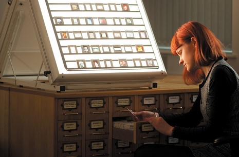 Student selecting slides from a drawer, their face is lit by the slide display.