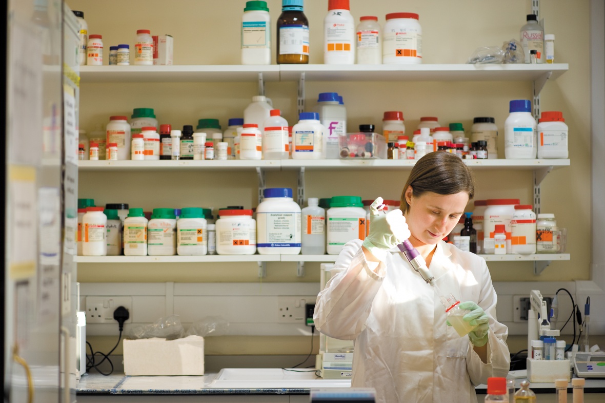 A stuent pipetting in front of a large selection of drugs and reagents