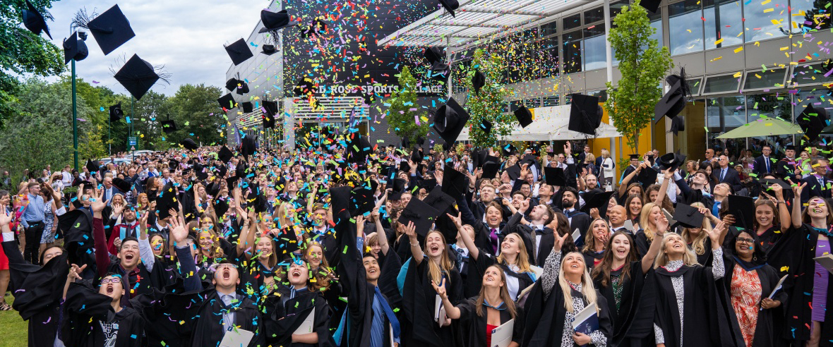 Graduates throwing their mortarboards into the air as confetti rains down