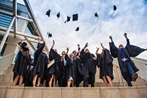 A group of students wear graduation gowns and through their hats in the air