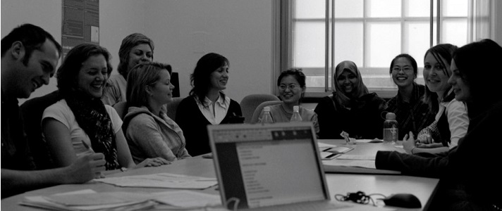 Black and white photo of a smiling group of people sat round a table with laptops and notebooks open in front of them