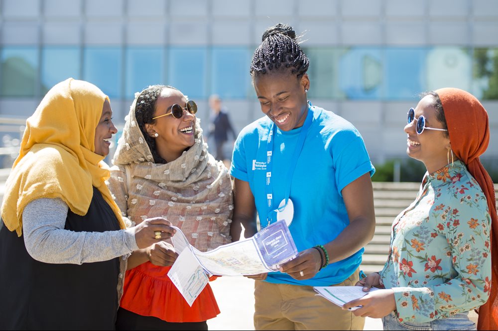 Young black student Helper with three female visitors wearing headscarves and sunglasses outside George Green Library.