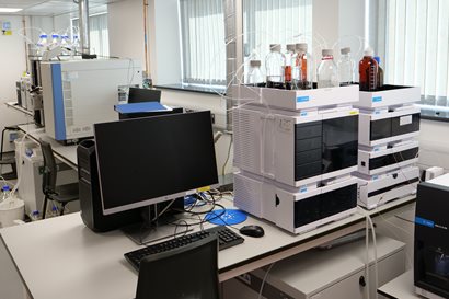 A desk in a laboratory with a large computer screen and an LCMS machine