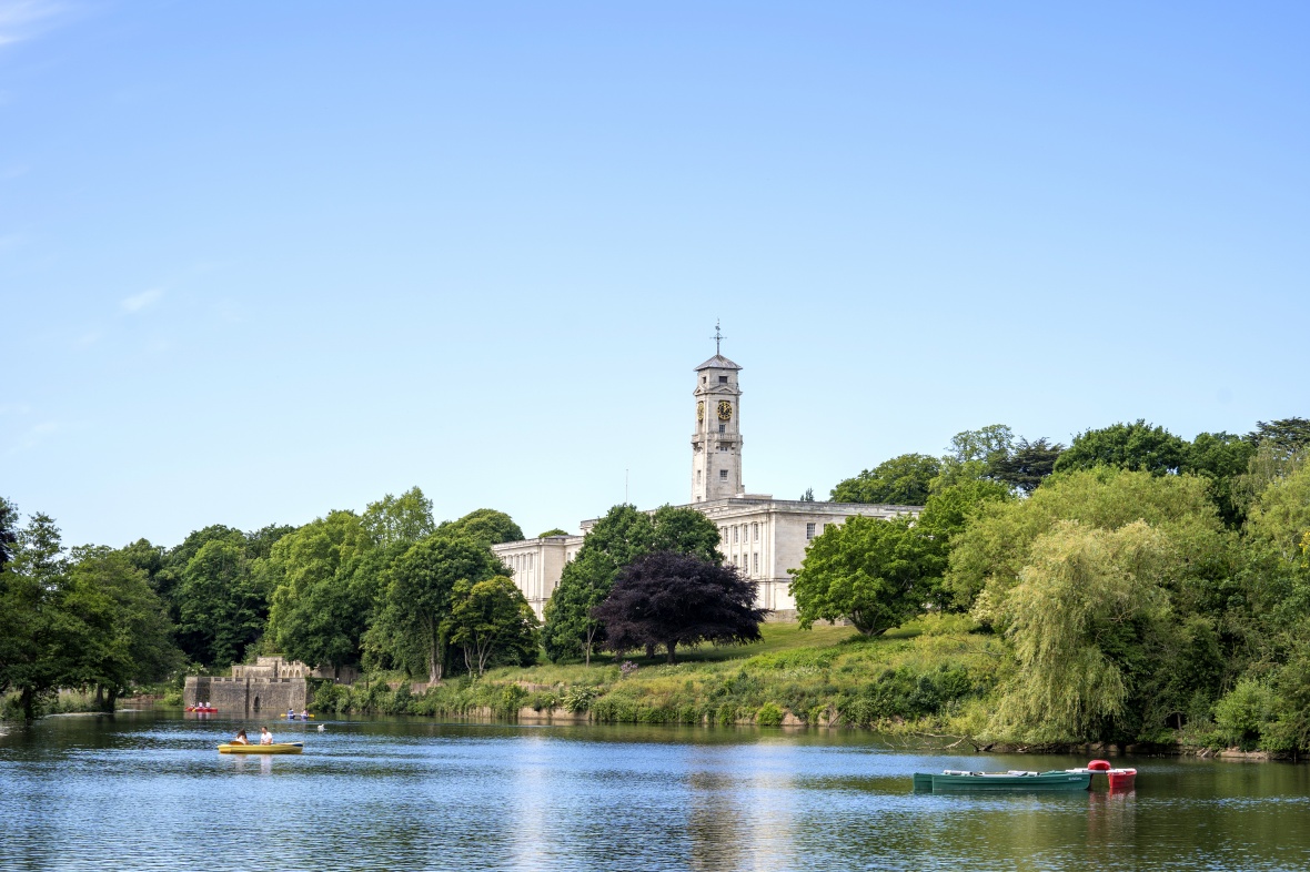 View of University of Nottingham's Trent Building and clock tower by a lake with people boating