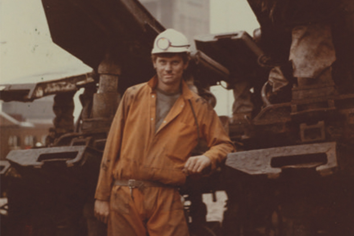Graham Kill in orange overalls standing near some mining equipment.