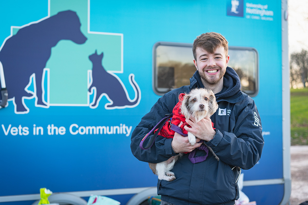 Veterinary student standing beside the Vets in the Community trailer while holding a dog.
