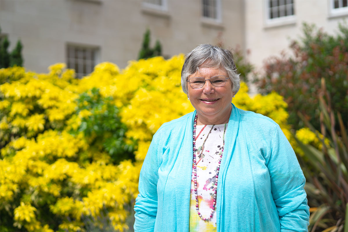 Jacky Hughes standing near some yellow flowers in the Trent Building courtyard.