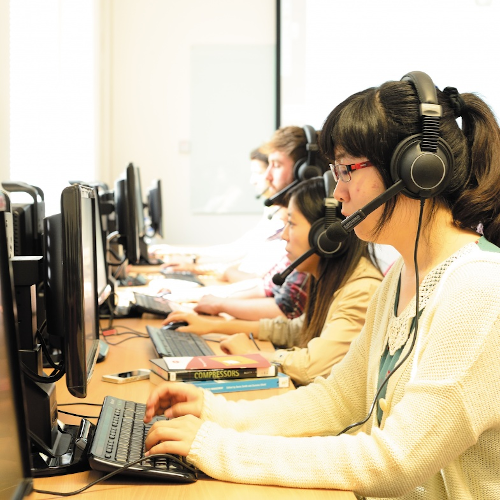 Students wearing headsets typing at computers in translation suite