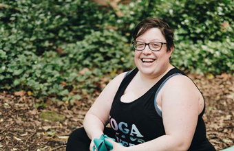 Miriam Zendle sitting smiling on a yoga mat in a forest