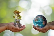 Two sets of hands the left one holding a glass jar filled with coins and a tree the right hands holding the earth.