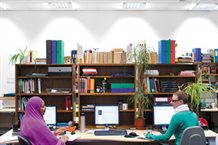 two postgraduate students sitting at their computers having a discussion