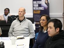 Avni Sondagar sits with other participants from the Help to Grow: Management course. They sit around a table and listen to a speaker off camera. Avni smiles.