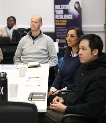 Avni Sondagar sits with other participants from the Help to Grow: Management course. They sit around a table and listen to a speaker off camera. Avni smiles.